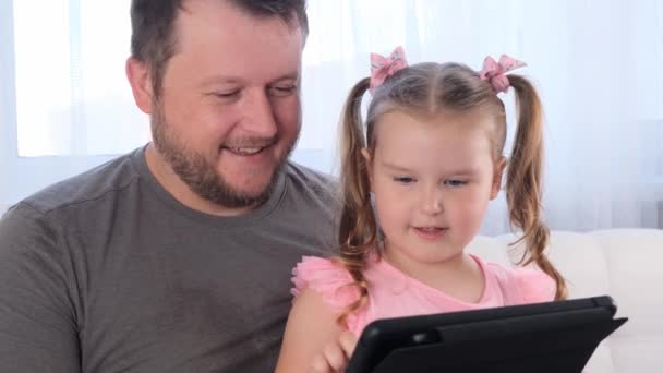 Riant petite fille de 3 ans et son père étudier ensemble sur une tablette et regarder une leçon en ligne à la maison. Papa aide sa fille avec ses études. Concept d'enseignement à distance en ligne. — Video