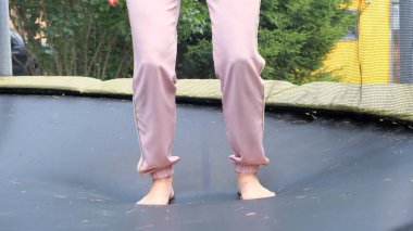 Genç bir kadın babutun üstüne atlıyor, yakın plan. Trambolinde zıpladıktan sonra bacaklar havada süzülür. Aile eğlencesi, eğlence ve spor, seçici odaklanma