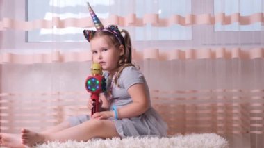 4-5 yaşlarında, kafasında bir çember ve elinde bir mikrofonla bir çocuk karaoke söylüyor, gelecekteki yüksek sesli solo müzisyenlerin katıldığı bir etkinlikte eğleniyor.