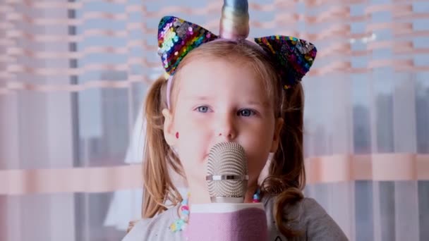 Смешная милая маленькая девочка 4-5 лет, поющая в караоке микрофон, с повязкой единорога, ребенок поет караоке музыку, весело провести время на мероприятии будущего музыканта громким голосом соло — стоковое видео