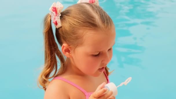 Drôle petite fille 4-5 ans, vêtue d'un maillot de bain rose, soufflant des boules de savon dans la piscine en vacances d'été — Video