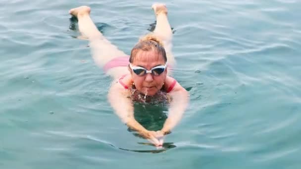 Woman aged 50-55-60 years old swims in the sea by a crawl. Professional swimmer, swimming race. Front crawl swimmer. Swimming lessons. — Stock Video