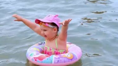 Komik küçük kız 3 yaşında şişme bir yüzükle, güneş şapkasıyla ve denizde yüzme gözlükleriyle yüzüyor. Yaz tatili konsepti, yüzme öğrenmek: Antalya, Manavgat Türkiye - 28 Temmuz 2021.
