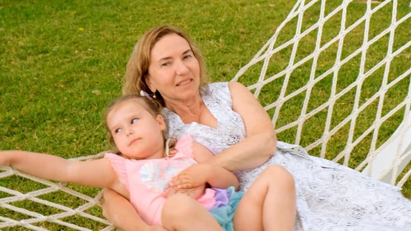 Carino coppia nonna e nipote 3 anni sono rilassanti e crogiolarsi in un'amaca su un prato verde nel loro giardino in una giornata di sole estivo. Concetto di vacanza, rapporto generazionale — Foto Stock