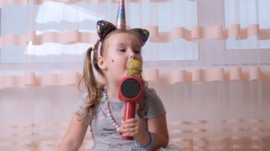 komik çekici çılgın bayan çocuk karaoke bir mikrofona şarkı söylüyor, tek boynuzlu at bandıyla, çocuk karaoke yapıyor, gelecek müzisyenlerin gürültülü seslerinde tek başına eğleniyor.