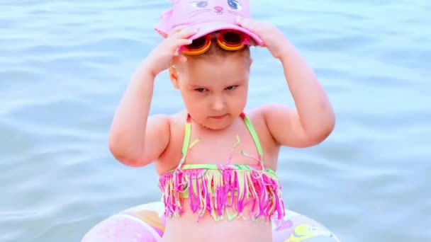 Komik küçük kız 3 yaşında şişme bir yüzükle, güneş şapkasıyla ve denizde yüzme gözlükleriyle yüzüyor. Yaz tatili konsepti, yüzme öğrenmek: Antalya, Manavgat Türkiye - 28 Temmuz 2021. — Stok video