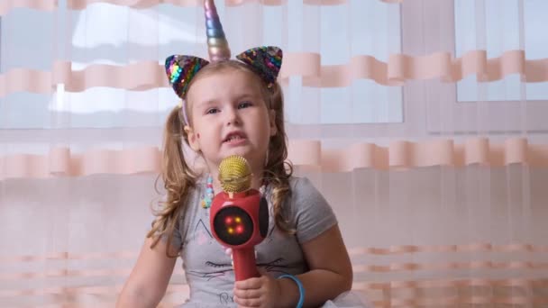 Engraçado bonito menina 4-5 anos, cantando em um microfone de karaoke, com uma faixa de cabeça de unicórnio, criança cantando música de karaoke, divirta-se em um evento futuro músico alta voz solo — Vídeo de Stock