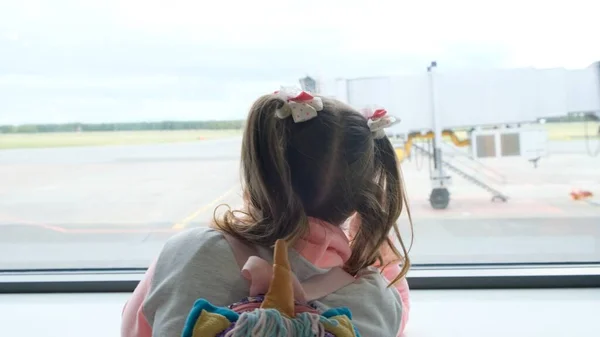 Liten flicka i åldern 5 år tittar ut genom fönstret på flygplatsen, väntar på avgång eller ankomst av planet, drömmer om en resa — Stockfoto