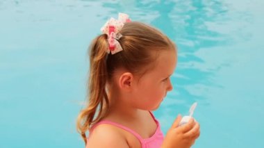 4-5 yaşlarında, at kuyruklu, pembe mayo giyen yaz tatilinde havuzda sabun topu üfleyen tatlı bir kız.