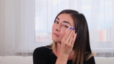 Dişi, kusursuz cildini beyaz pamuklu süngerle temizliyor. Genç bir kadın yüzüne bakar. Spa ve sağlık, cilt bakımı konsepti. Kişisel bakım