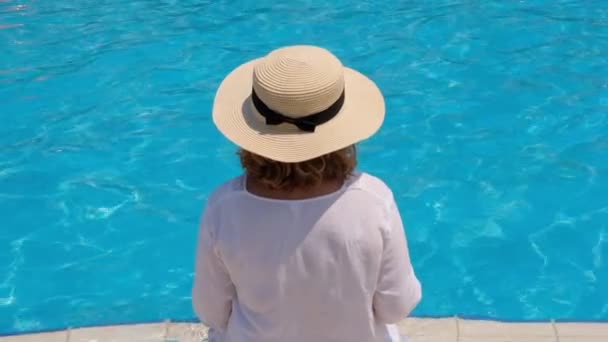 Mulher sênior relaxante perto dos hotéis piscina exterior azul. As pessoas estão desfrutando suas férias de verão. Tudo incluído, vista traseira — Vídeo de Stock