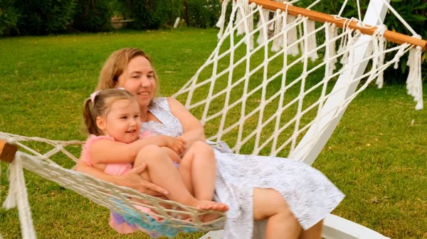 Coppia nonna e nipote di 3 anni sono rilassanti e crogiolarsi in un'amaca su un prato verde nel loro giardino in una giornata di sole estivo. Concetto di vacanza, relazione generazionale, genitorialità — Foto Stock