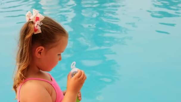 Grappig klein meisje 4-5 jaar oud, gekleed in een roze badpak, blazen zeep ballen in het zwembad op zomervakantie — Stockvideo