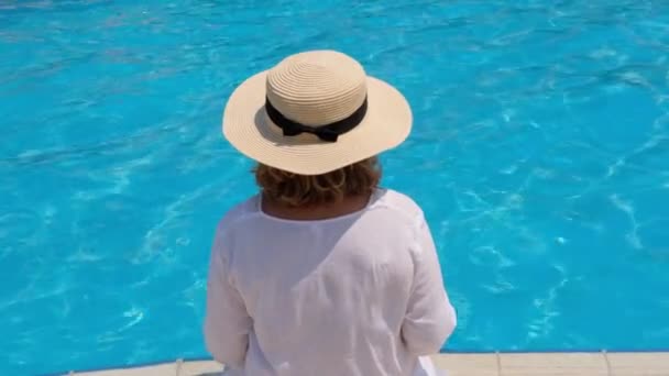 Старша жінка розслабляється біля готелів блакитний відкритий басейн. Люди насолоджуються літніми канікулами. Все включено, вид ззаду — стокове відео
