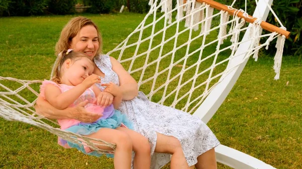 Avó e neta, 3 anos de idade, descansar e desfrutar de uma rede em um prado verde em seu jardim em um dia ensolarado de verão. Conceito de férias, relacionamento geracional, parentalidade, infância feliz. — Fotografia de Stock