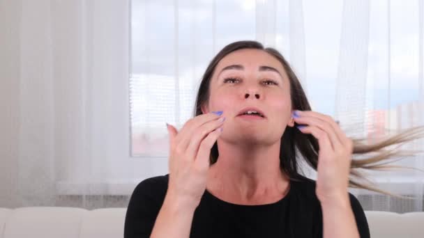 Гарна брюнетка жінка робить собі масаж обличчя вздовж ліній масажу і вказує руками. Масаж обличчя. Гімнастика обличчя. Система вправ покращує шкіру самостійно — стокове відео