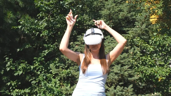 Mulher vestindo óculos de realidade virtual dança contra o fundo de árvores verdes, representando a realização de um sonho. O conceito de obter experiência usando óculos de fone de ouvido VR de virtual — Fotografia de Stock