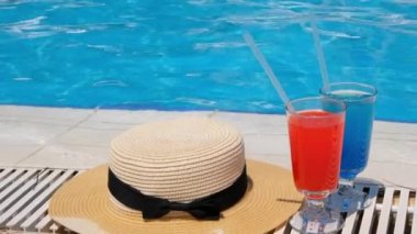 İki renkli kokteyl bardağı pembe ve mavi, yüzme havuzunun kenarında güneş şapkası, yakın çekim. Spa Otel 'de tatil ve rahatlama konsepti
