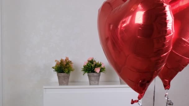 Twee rode hartvormige ballonnen in de woonkamer tegen de achtergrond van een witte ladekast. Vakantie concept, decoratie, cadeau, Valentijnsdag — Stockvideo