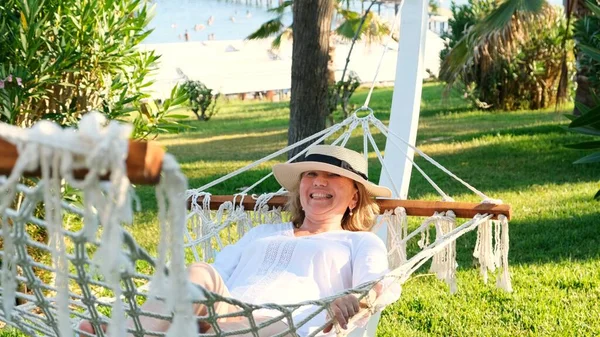 Hasır şapkalı yaşlı kadın palmiye ağaçlarının etrafındaki bir hamakta dinleniyor ve huzur ve rahatlığın tadını çıkarıyor. Yaşlılar yaşam tarzı konsepti