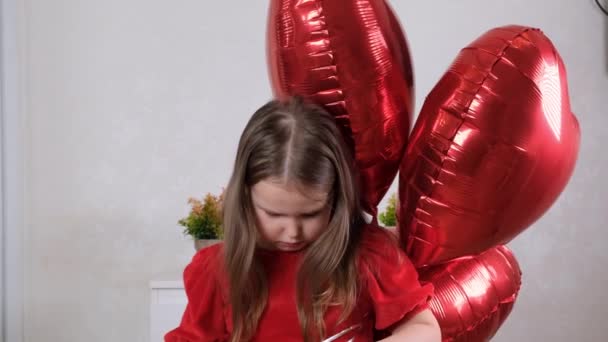 Szomorú kislány piros ruhában, három szív alakú lufival Valentin napra. A család szeretete. ajándékok az ünnepre. boldogság és csók — Stock videók