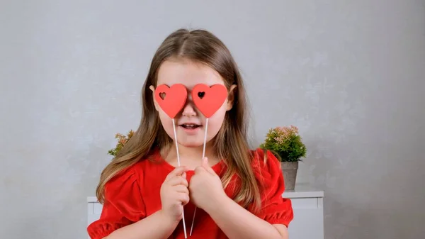 面白い棒の上に2つの心を持つ赤いドレスのかなり小さな女の子は彼らと彼女の目を閉じます。バレンタインデーのコンセプト. — ストック写真