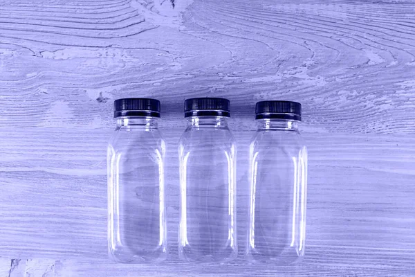 Três garrafas vazias transparentes de plástico com uma tampa preta em uma mesa de madeira. Há um lugar para o seu logotipo. Imagem muito tonificada de Peri. espaço de cópia — Fotografia de Stock