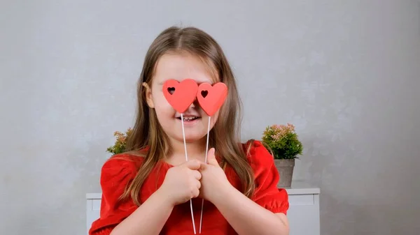 面白い棒の上に2つの心を持つ赤いドレスのかなり小さな女の子は彼らと彼女の目を閉じます。バレンタインデーのコンセプト. — ストック写真
