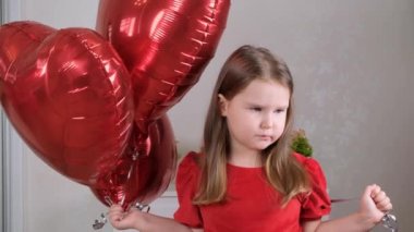 Sevgililer günü için üç kalp şeklinde balonları olan kırmızı elbiseli üzgün küçük kız. Aile sevgisi. Tatil için hediyeler. mutluluk ve öpücükler
