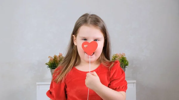 Drôle Petite fille dans une robe rouge avec un coeur sur un bâton ferme les yeux. Concept de Saint-Valentin. — Photo