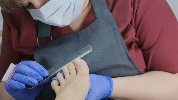 Empleado del salón de pedicura utiliza una lima de uñas durante un tratamiento del dedo del pie. Primer plano, enfoque selectivo. —  Fotos de Stock