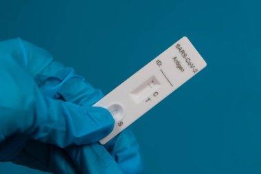 Koruyucu bir tıbbi eldiven içinde mavi bir arka planda negatif SARS-CoV-2 Hızlı Antijen Testi bulunur.