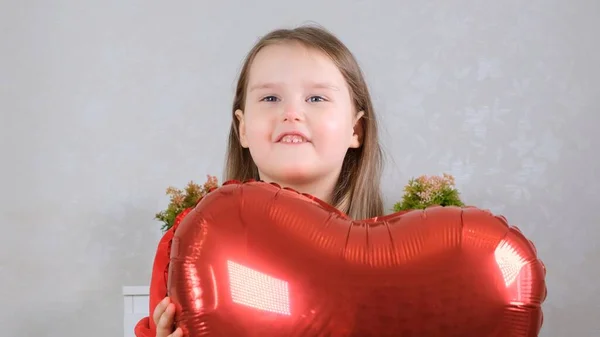 Mała słodka dziewczyna w czerwonej sukience chowa się za czerwonym kształcie serca balon. Koncepcja Walentynki — Zdjęcie stockowe