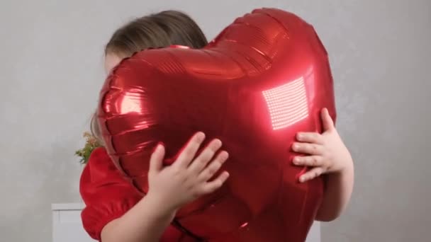 Little cute girl in a red dress gently hugs red heart shaped balloons with her hands. valentines day concept — Stock Video