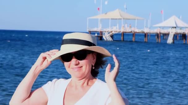 青い海の背景にわらの帽子とサングラスを着用し、成熟した女性、年齢50の肖像画。夏休み休暇現役引退者 — ストック動画