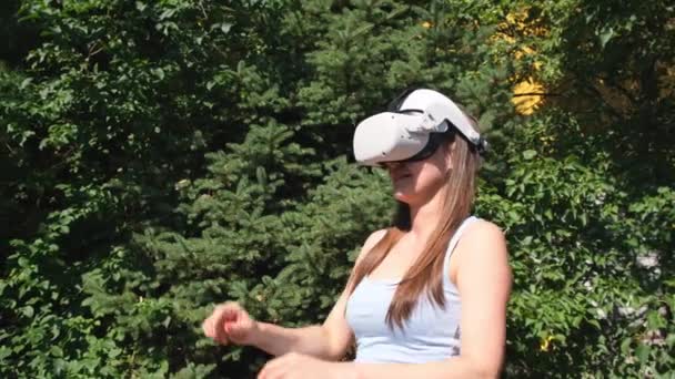 在绿树成荫的背景下，戴着虚拟现实眼镜的女性用手控制着这个装置 — 图库视频影像