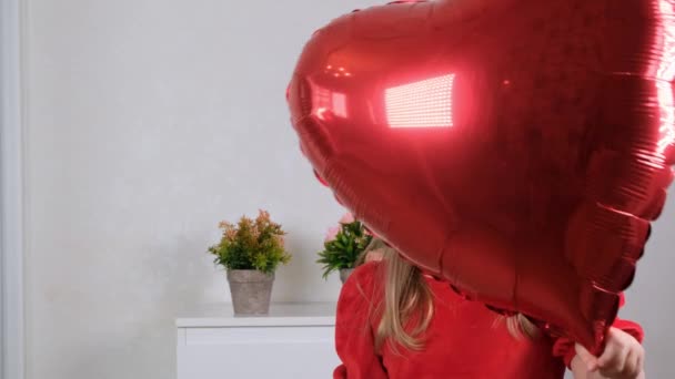 Gadis kecil yang lucu dengan gaun merah bersembunyi di balik balon berbentuk hati merah. konsep hari valentine — Stok Video