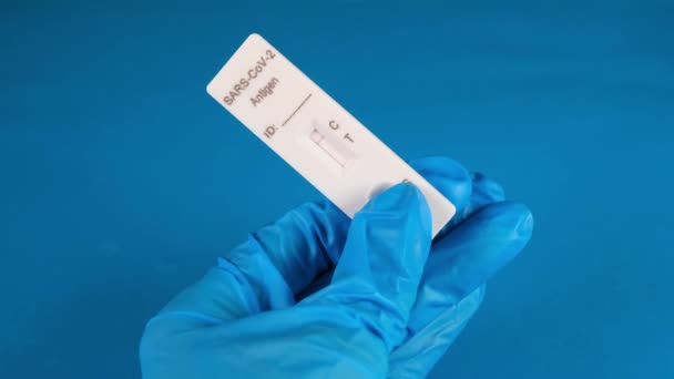 Handen i en skyddande medicinsk handske håller en negativ SARS-CoV-2 Rapid Antigen Test på en blå bakgrund — Stockvideo