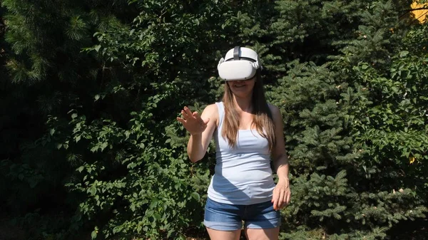 Женщина в очках виртуальной реальности управляет устройством руками на фоне зеленых деревьев — стоковое фото