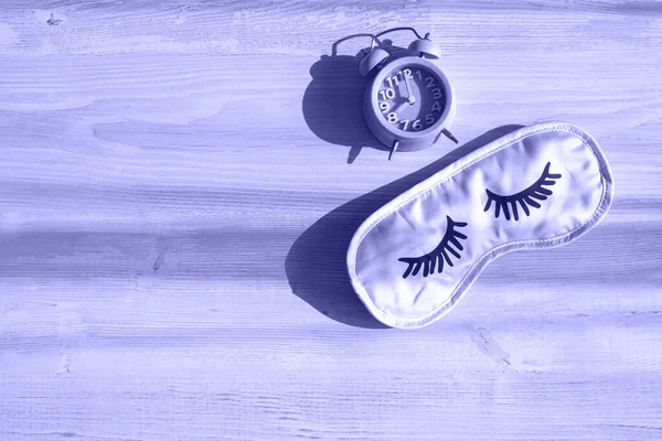 Despertador e máscara de sono em uma mesa branca de madeira na luz solar da manhã. O conceito de começar um novo dia, bom dia ou terminar o dia, tarde da noite. Planejamento. Imagem muito tonificada de Peri. Cópia — Fotografia de Stock