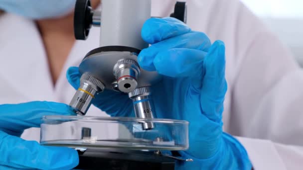 Руки дослідника-лаборанта в захисних рукавичках, що тримають мікроскоп в лабораторії, крупним планом . — стокове відео