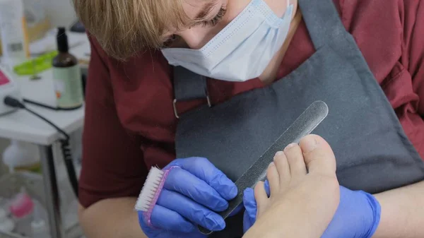 Pedikür salonu çalışanı ayak parmağı tedavisi sırasında tırnak törpüsü kullanır. Yaklaş, seçici odaklanma. — Stok fotoğraf