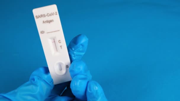 Tangan di sarung tangan medis pelindung memegang Negatif SARS-CoV-2 Rapid Antigen Test pada latar belakang biru — Stok Video