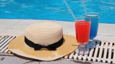 İki renkli kokteyl bardağı pembe ve mavi, yüzme havuzunun kenarında güneş şapkası, yakın çekim. tatil tropikal konsepti