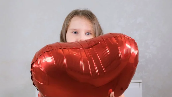 Mała słodka dziewczyna w czerwonej sukience chowa się za czerwonym kształcie serca balon. Koncepcja Walentynki — Zdjęcie stockowe