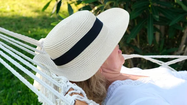 Жінка в солом'яному капелюсі відпочиває в гамаку навколо пальми і насолоджується спокоєм і релаксацією. Концепція відпустки — стокове фото