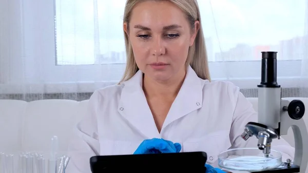 Químico de pesquisa de cientista profissional com um computador tablet e um microscópio realiza pesquisa em laboratório. — Fotografia de Stock