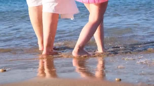 Bedstemor og barnebarn går langs kysten og plasker i havet med fødderne på en varm sommersolskinsdag. Begrebet sommerferie, sjov, familie – Stock-video
