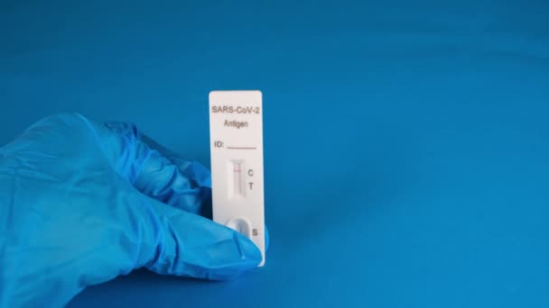 Χέρι σε ένα προστατευτικό ιατρικό γάντι κρατά ένα αρνητικό SARS-CoV-2 Ταχεία δοκιμή αντιγόνων σε μπλε φόντο — Αρχείο Βίντεο