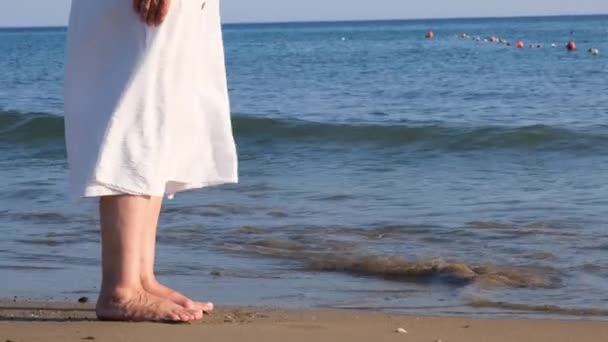 Mature female legs are walking along the sandy beach and splashing in the sea on a summer sunny day. Woman walks barefoot on the water close-up — Stock Video